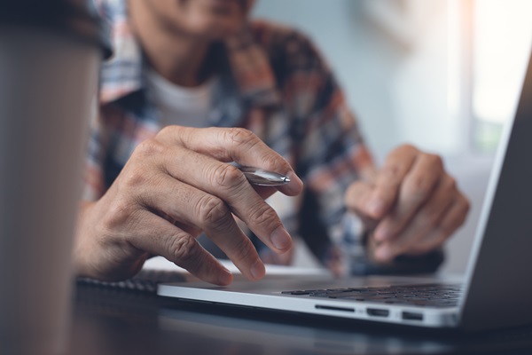 Man looking at laptop holding a pen